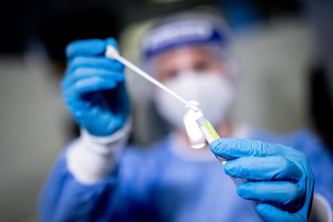Eine Frau hält in einem Corona-Testcenter die Probe von einem Rachenabstrich in den Händen. Symbolfoto: dpa