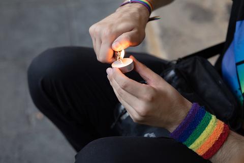 Ein Mann entzündet eine Kerze in Gedenken an Malte C.. Er trägt ein Schweißband in den Farben des Regenbogens als ein Symbol der LGBT-Bewegung.  Foto: Friso Gentsch/dpa