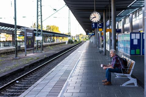 Ein Mann sitzt mit einem Kaffee in der Hand auf einer Bank auf dem ansonsten menschenleeren Bahnsteig. Foto: dpa/Philipp von Ditfurt
