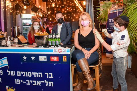 Eine junge Frau wird vor einer Bar am Dizengoff Platz im Zentrum der Stadt  geimpft. Die Stadtverwaltung von Tel Aviv bietet jedem, der sich dort impfen lässt, ein Freigetränk an. Israels Regierung will so schnell wie möglich so viele Menschen wie möglich impfen, um die Corona-Krise hinter sich zu lassen. Foto: Kfir Sivan/Tel Aviv-Yafo Municipality/dpa