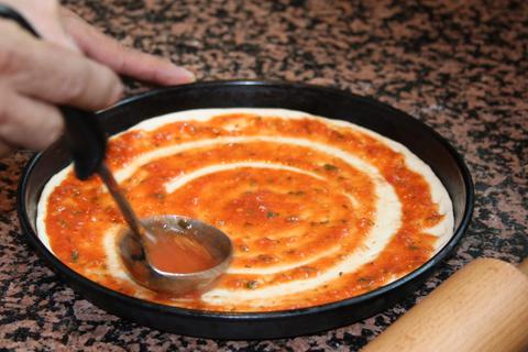 Eine Pizza wird mit Sauce bestrichen. Foto: adobe.stock/lafota