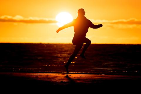 Ein Mädchen springt vor der untergehenden Sonne am Strand. Foto: dpa