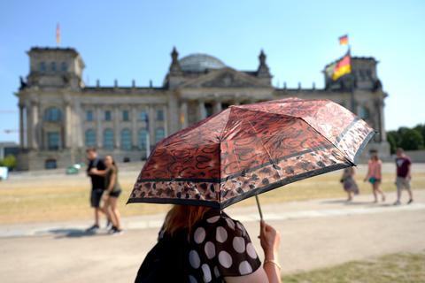 Mit einem Schirm schützt sich eine Frau am Reichstag in Berlin bei Temperaturen um 35 Grad vor der Sonne (Archivbild vom 27.07.2013). 